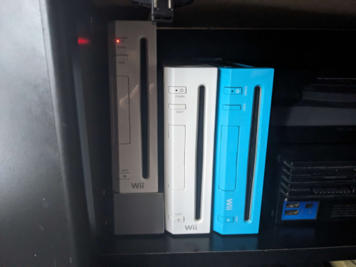 three wiis, two white and one blue, side by side inside of a tv console.